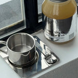 Jar of broth and metal cup on a reflective surface with a window in the background